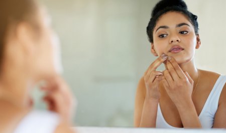 Mujer mirándose al espejo con problemas de acné en la piel 