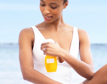 Woman with black skin using SPF50+ Sunscreen Spray compatible for the whole family